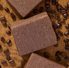 Dark goat milk soap bars on a wooden surface with coffee beans