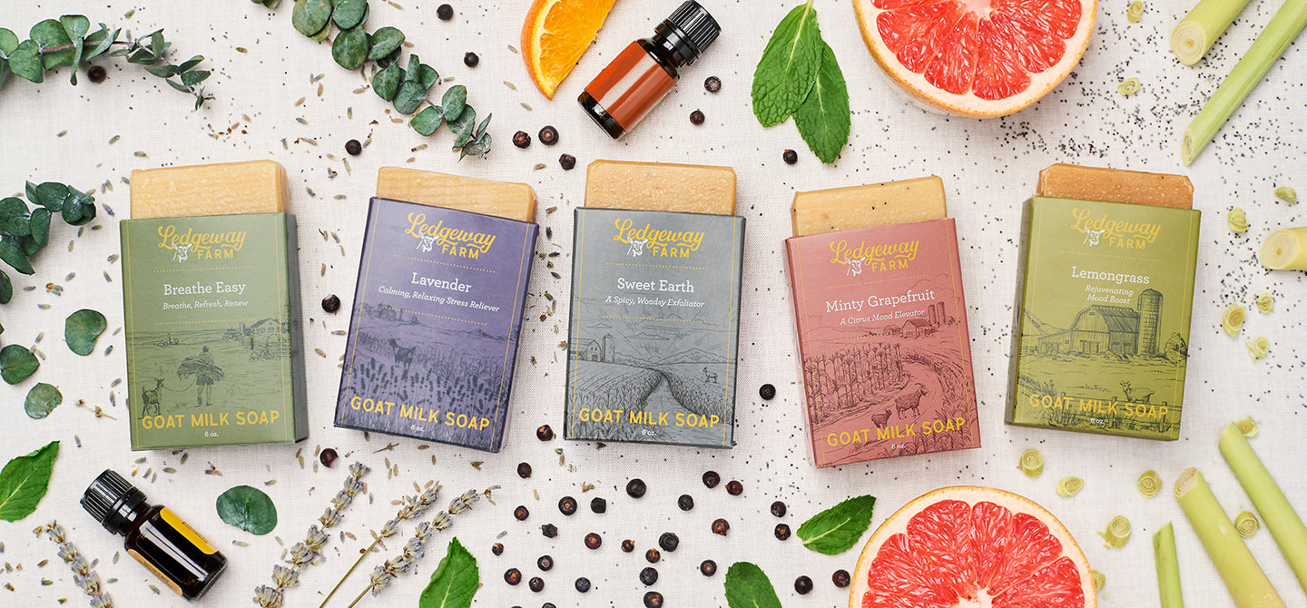 Five bars of Ledgeway Farm goat milk soap on a textured surface with herbs and fruits.