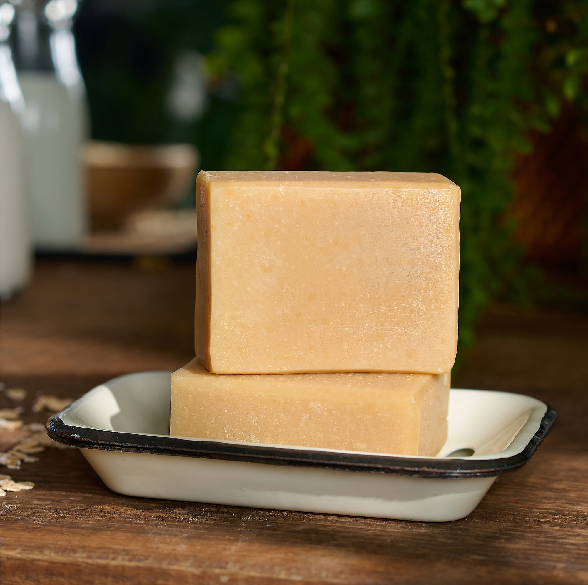 Two bars of soap stacked on a white tray with a blurred natural background