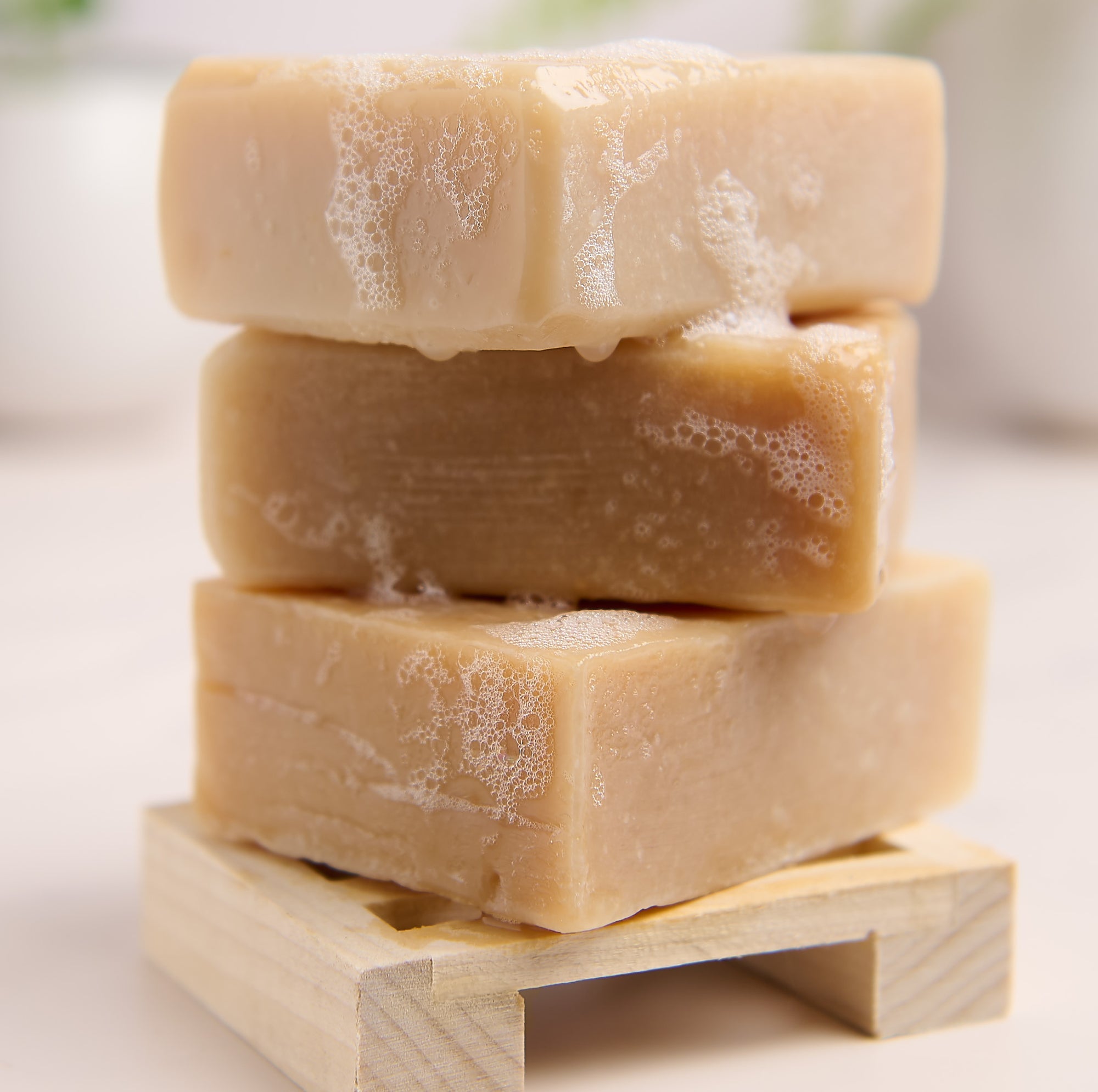 Stack of three bars of soap on a wooden block with a blurred background