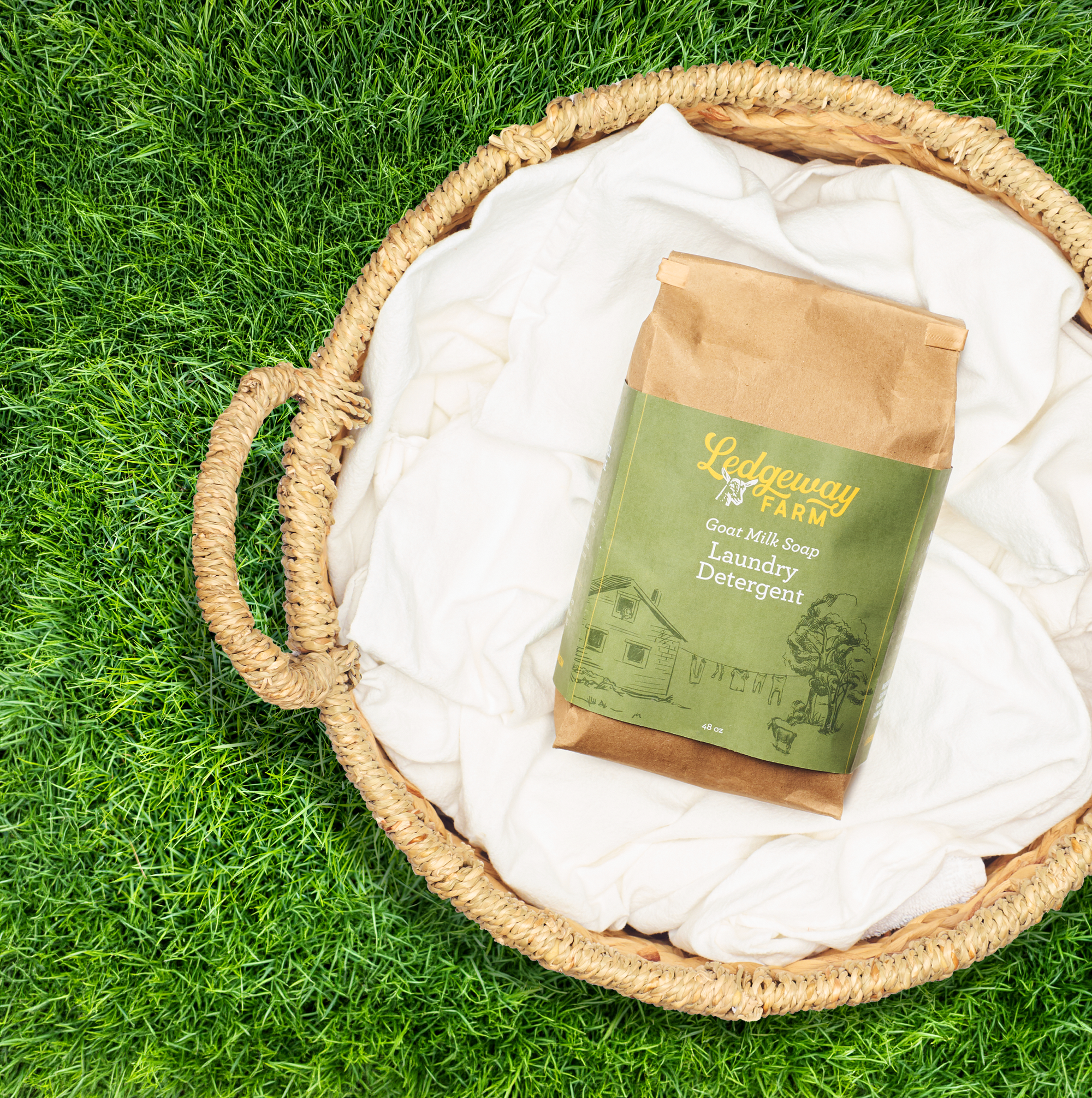 Basket with laundry detergent and white towels on grass